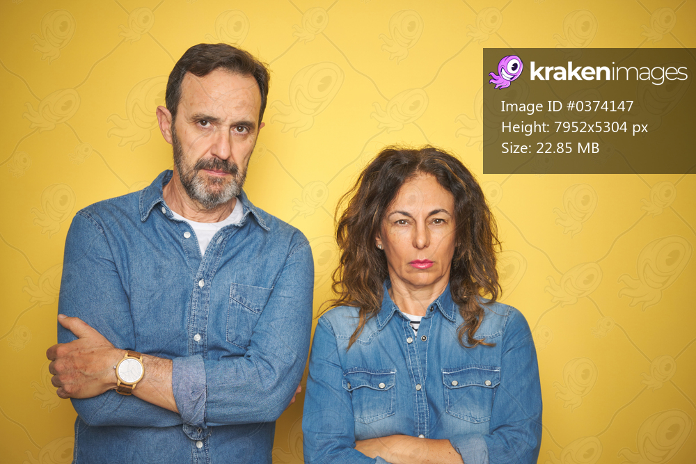 Beautiful middle age couple together standing over isolated yellow background skeptic and nervous, disapproving expression on face with crossed arms. Negative person.