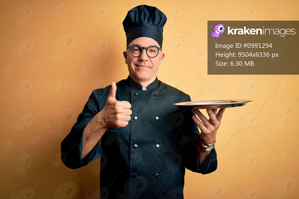 Middle age handsome grey-haired waiter man wearing cooker uniform and hat holding tray happy with big smile doing ok sign, thumb up with fingers, excellent sign