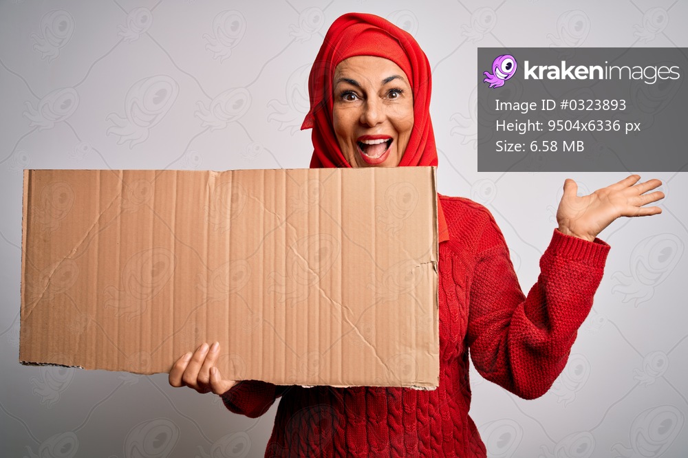 Middle age brunette woman wearing traditional muslim hijab holding banner very happy and excited, winner expression celebrating victory screaming with big smile and raised hands