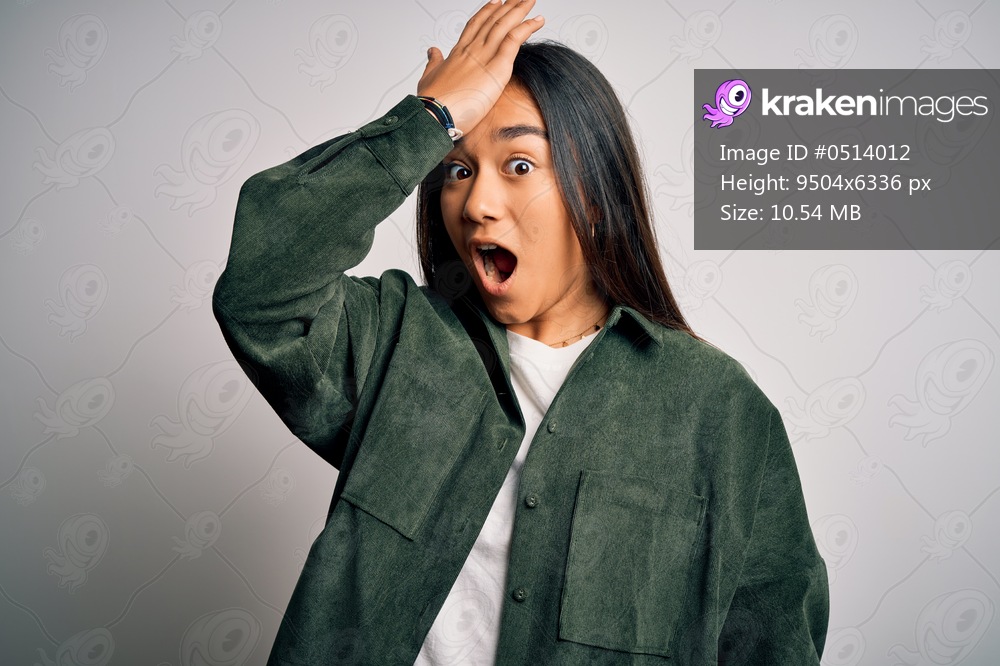 Young beautiful asian woman wearing casual shirt standing over isolated white background surprised with hand on head for mistake, remember error. Forgot, bad memory concept.