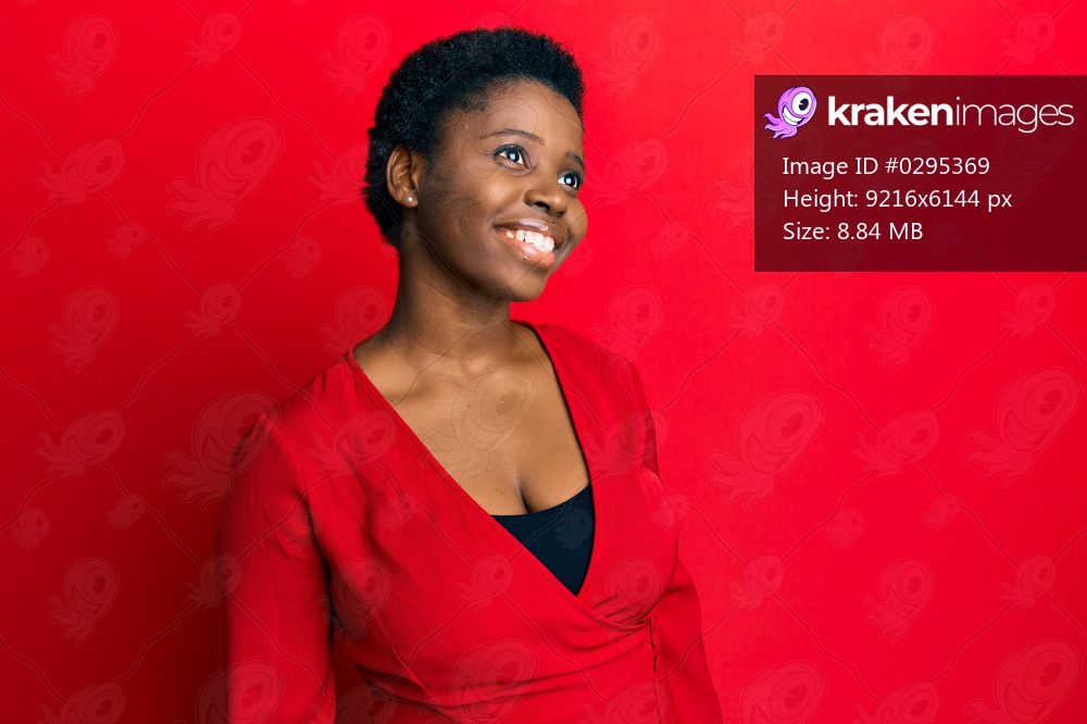 Young african woman with afro hair wearing casual clothes over red background looking to side, relax profile pose with natural face and confident smile. 