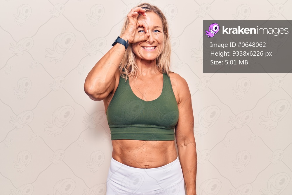 Middle age caucasian blonde woman wearing sportswear doing ok gesture with hand smiling, eye looking through fingers with happy face. 