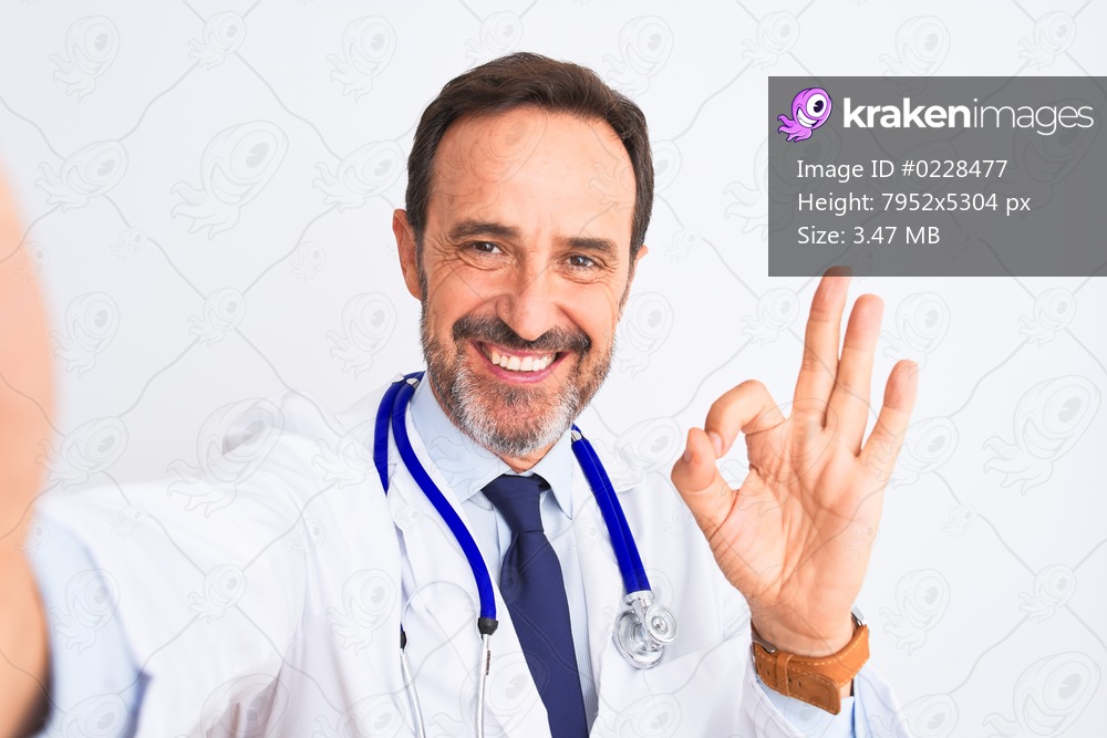 Middle age doctor man wearing stethoscope make selfie over isolated white background doing ok sign with fingers, excellent symbol