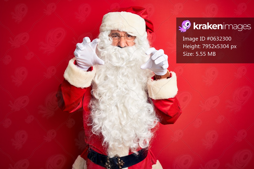 Middle age handsome man wearing Santa costume standing over isolated red background smiling funny doing claw gesture as cat, aggressive and sexy expression