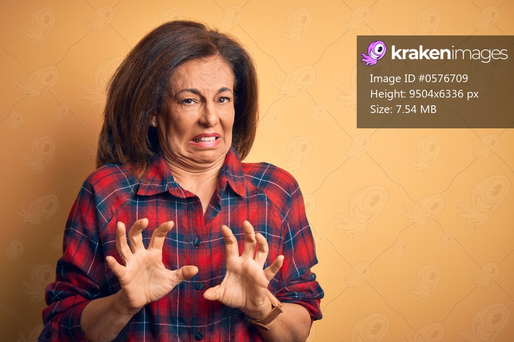Middle age beautiful woman wearing casual shirt standing over isolated yellow background disgusted expression, displeased and fearful doing disgust face because aversion reaction.