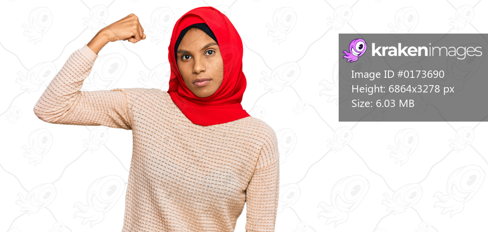 Young african american woman wearing traditional islamic hijab scarf strong person showing arm muscle, confident and proud of power 