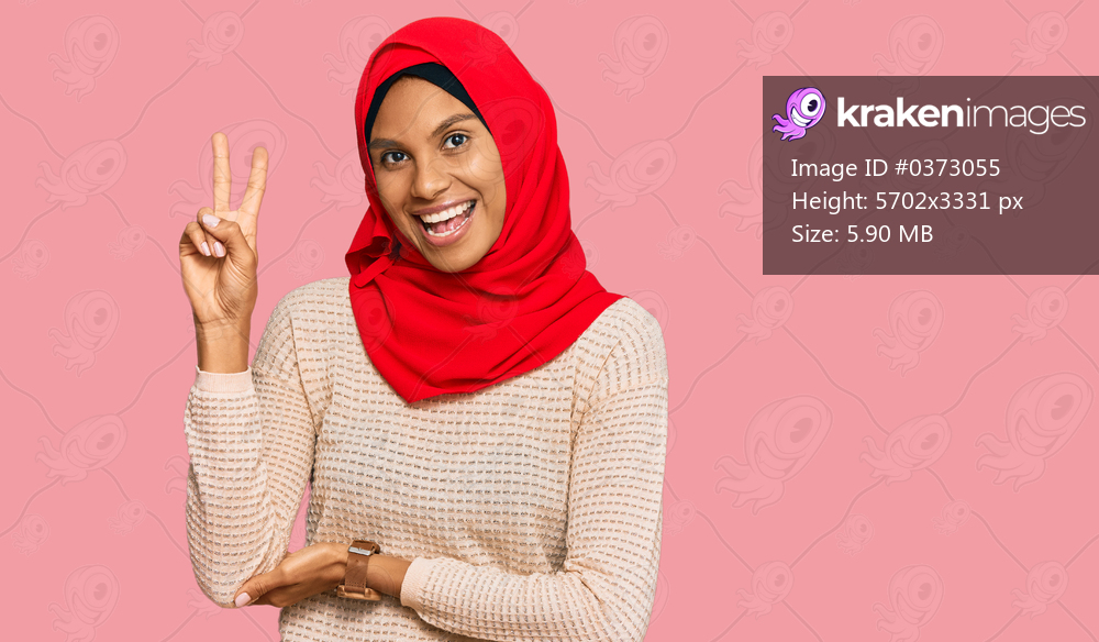 Young african american woman wearing traditional islamic hijab scarf smiling with happy face winking at the camera doing victory sign with fingers. number two. 