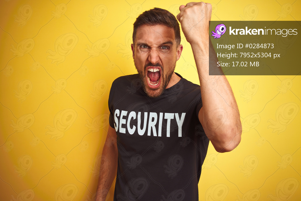Young safeguard man wearing security uniform over yellow isolated background angry and mad raising fist frustrated and furious while shouting with anger. Rage and aggressive concept.