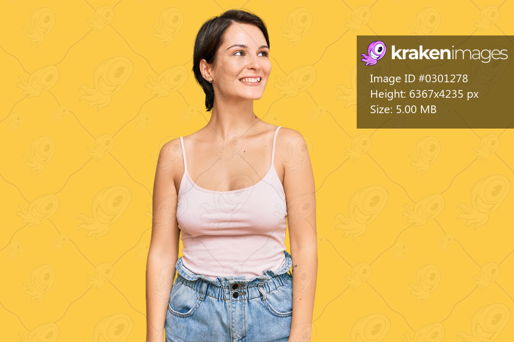 Young brunette woman with short hair wearing casual summer clothes looking away to side with smile on face, natural expression. laughing confident. 