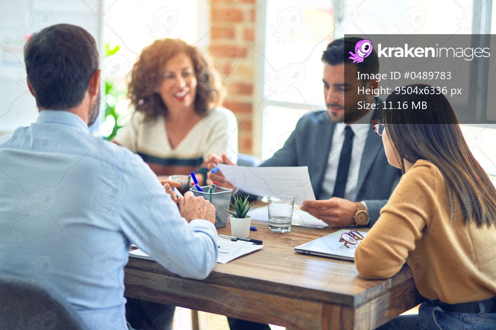Group of business workers smiling happy working together. Sitting on desk with smile on face reading documents at the office