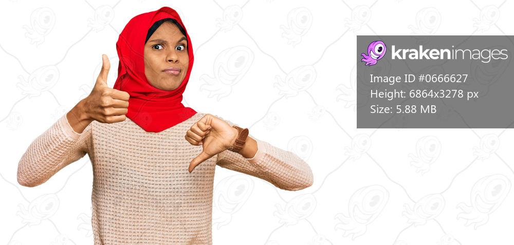Young african american woman wearing traditional islamic hijab scarf doing thumbs up and down, disagreement and agreement expression. crazy conflict 