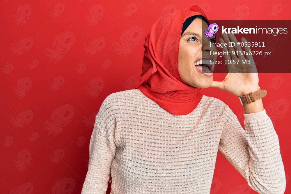 Young african american woman wearing traditional islamic hijab scarf shouting and screaming loud to side with hand on mouth. communication concept. 