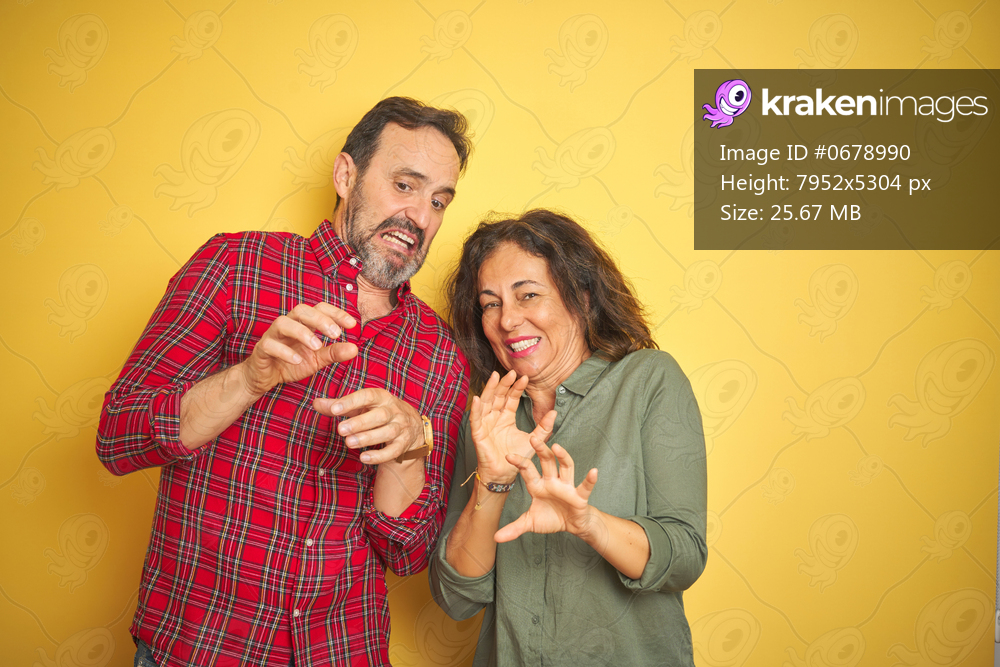 Beautiful middle age couple over isolated yellow background disgusted expression, displeased and fearful doing disgust face because aversion reaction. With hands raised. Annoying concept.