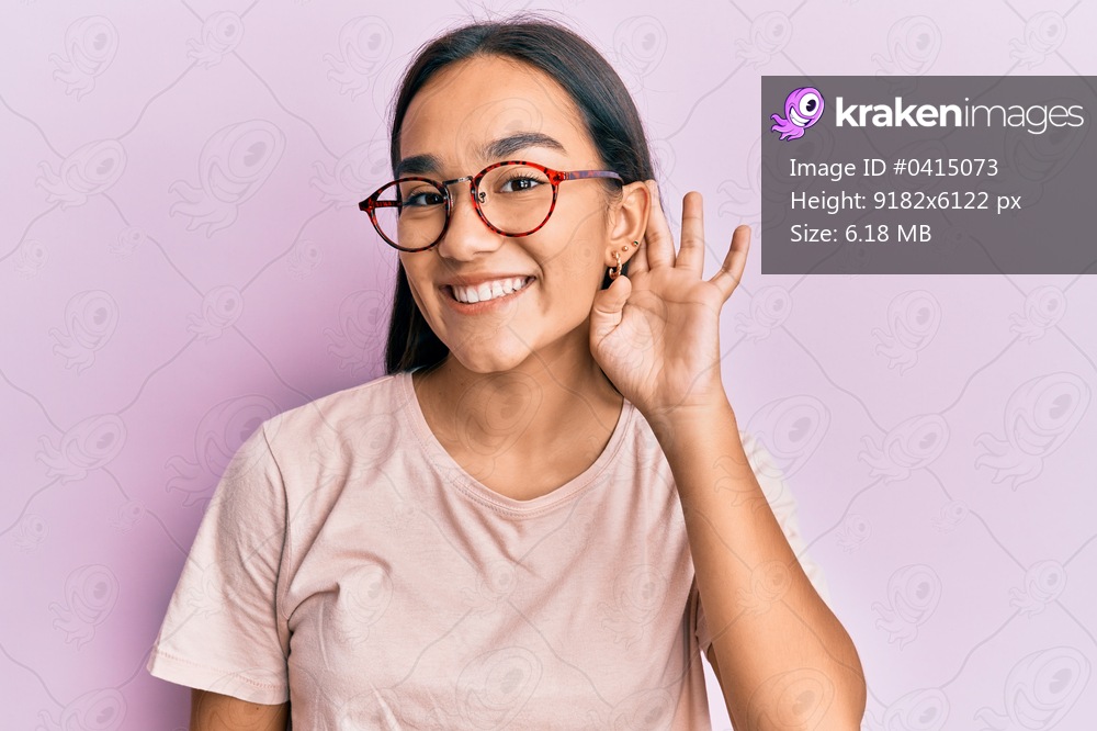 Young asian woman wearing casual clothes and glasses smiling with hand over ear listening and hearing to rumor or gossip. deafness concept. 