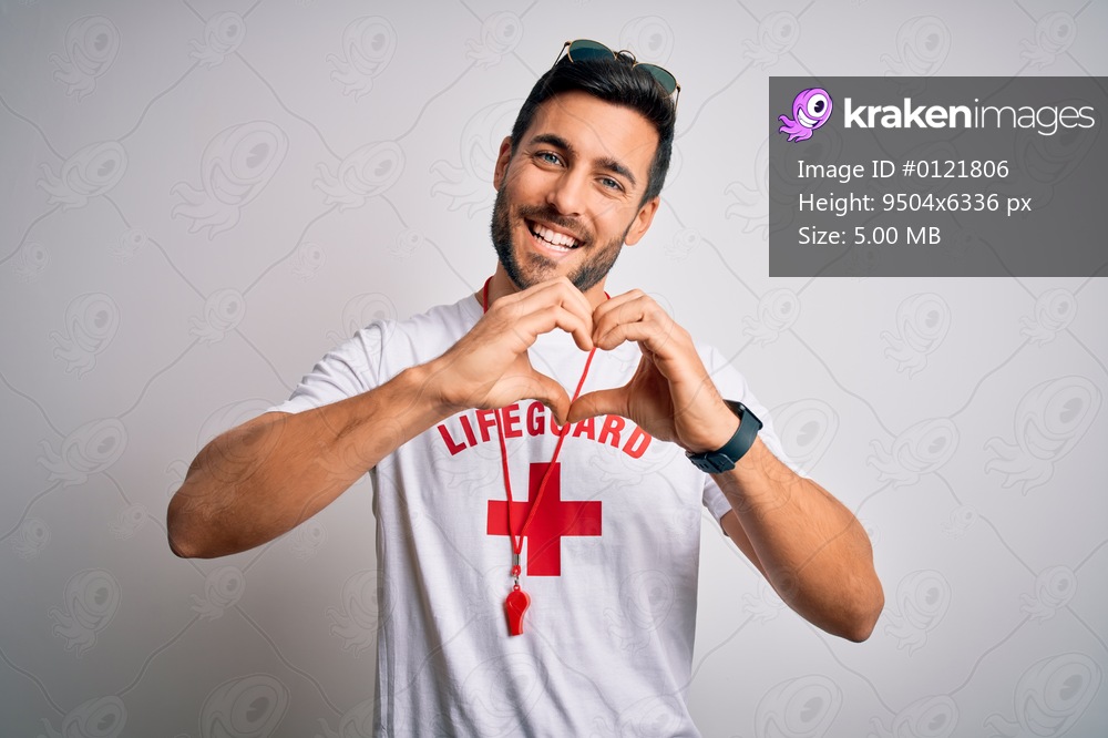 Young handsome lifeguard man with beard wearing t-shirt with red cross and whistle smiling in love doing heart symbol shape with hands. Romantic concept.