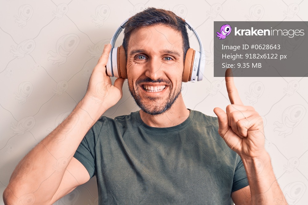 Young handsome man listening to music using headphones over isolated white background smiling with an idea or question pointing finger with happy face, number one