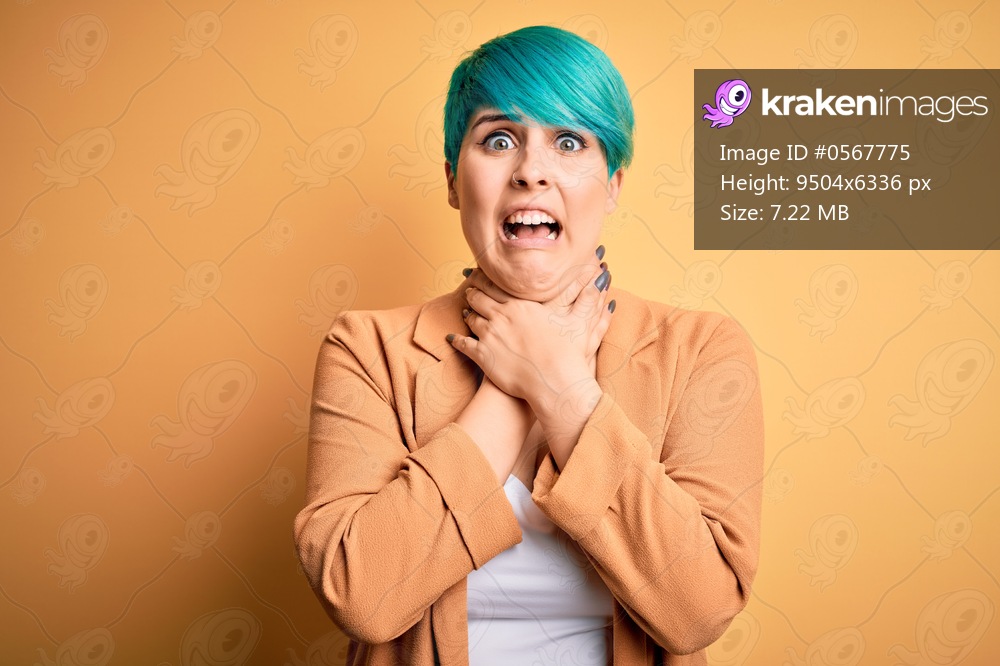 Young beautiful woman with blue fashion hair wearing casual jacket over yellow background shouting and suffocate because painful strangle. Health problem. Asphyxiate and suicide concept.