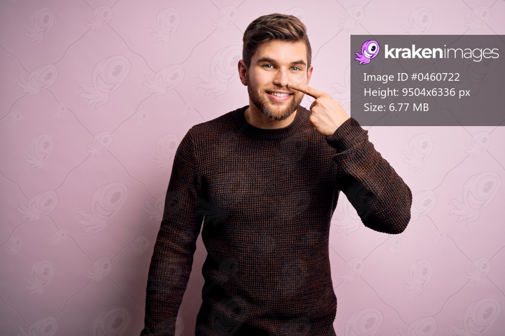 Young blond man with beard and blue eyes wearing casual sweater over pink background Pointing with hand finger to face and nose, smiling cheerful. Beauty concept