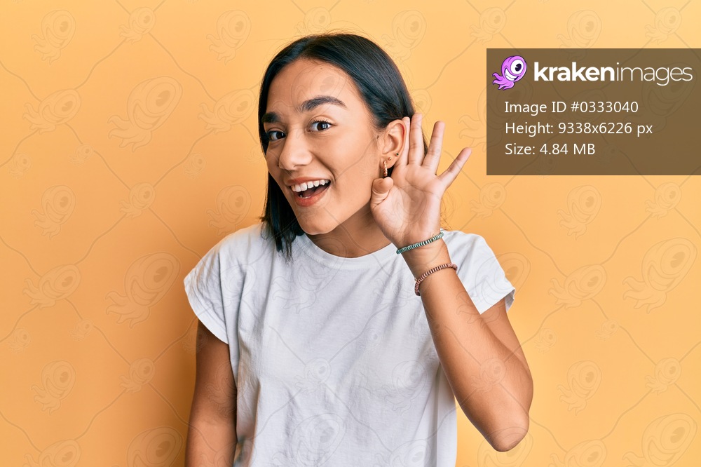 Young asian woman wearing casual white t shirt smiling with hand over ear listening and hearing to rumor or gossip. deafness concept. 