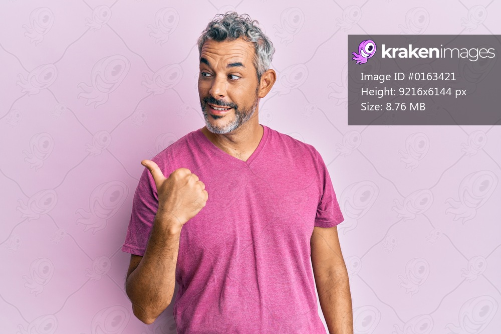 Middle age grey-haired man wearing casual clothes smiling with happy face looking and pointing to the side with thumb up. 