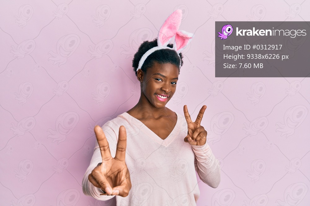 Young african american girl wearing cute easter bunny ears smiling looking to the camera showing fingers doing victory sign. number two. 