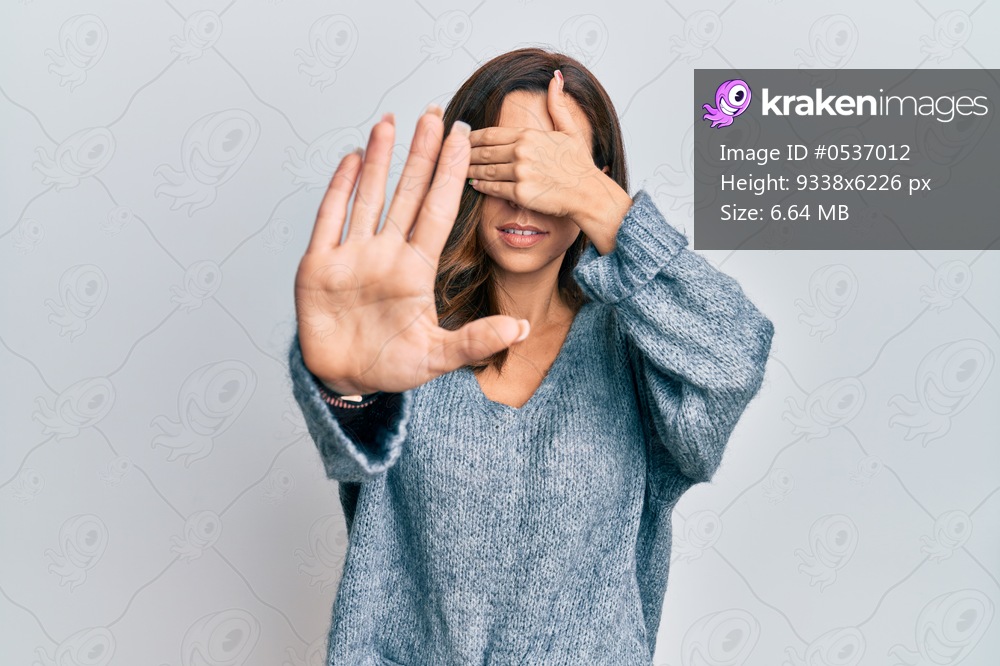 Young brunette woman wearing casual winter sweater covering eyes with hands and doing stop gesture with sad and fear expression. embarrassed and negative concept. 