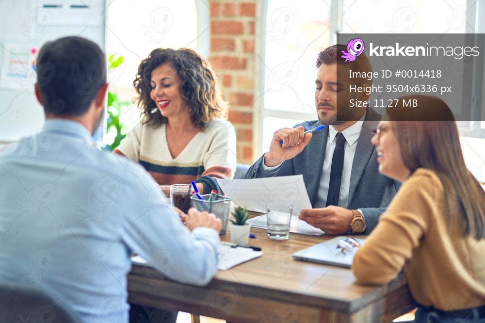Group of business workers smiling happy working together. Sitting on desk with smile on face reading documents at the office
