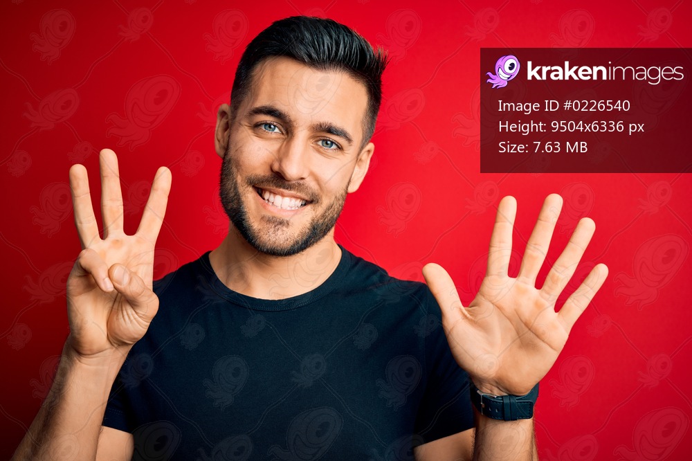 Young handsome man wearing casual black t-shirt standing over isolated red background showing and pointing up with fingers number eight while smiling confident and happy.