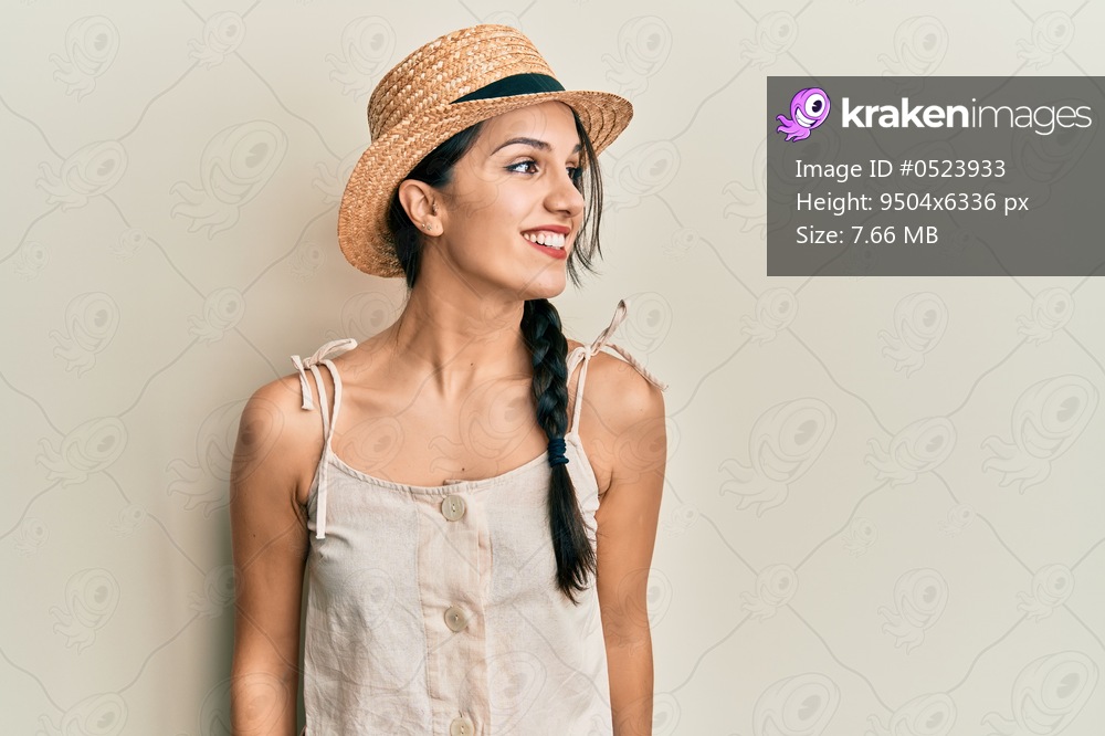 Young hispanic woman wearing summer hat looking to side, relax profile pose with natural face and confident smile. 