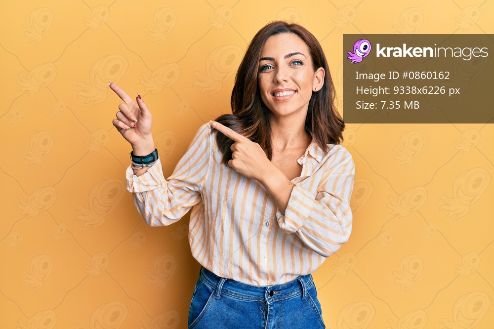 Young brunette woman wearing casual clothes over yellow background smiling and looking at the camera pointing with two hands and fingers to the side. 