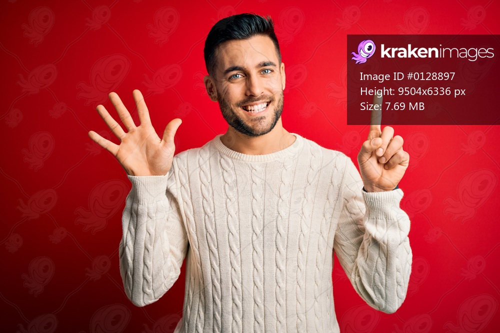 Young handsome man wearing casual white sweater standing over isolated red background showing and pointing up with fingers number six while smiling confident and happy.