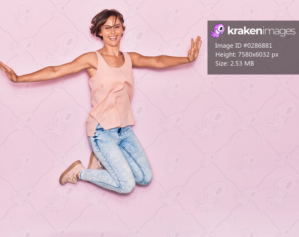 Young beautiful woman wearing casual clothes smiling happy. Jumping with smile on face and arms opened over isolated pink background.