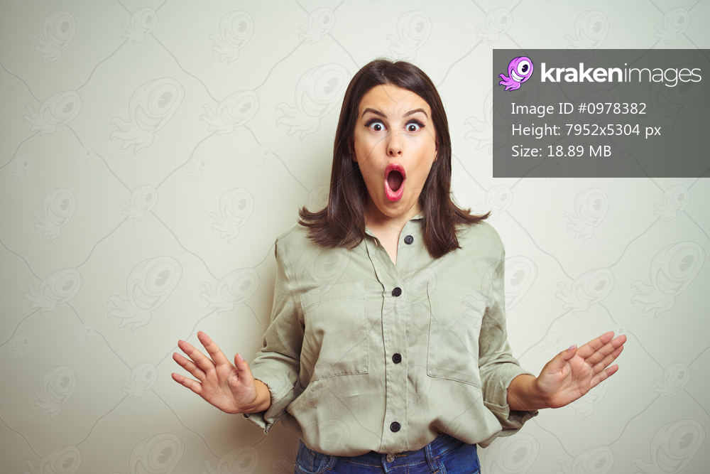 Young beautiful brunette woman wearing green shirt over isolated background afraid and shocked with surprise expression, fear and excited face.