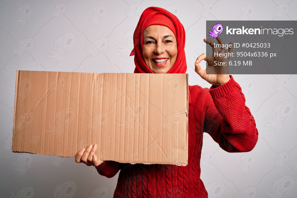 Middle age brunette woman wearing traditional muslim hijab holding banner doing ok sign with fingers, excellent symbol