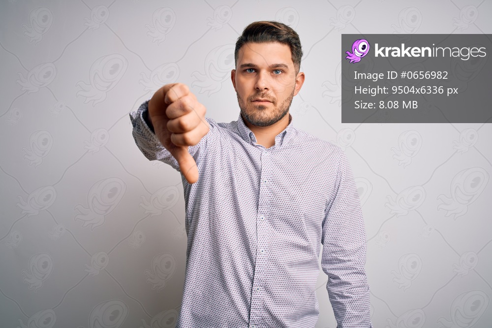 Young business man with blue eyes standing over isolated background looking unhappy and angry showing rejection and negative with thumbs down gesture. Bad expression.