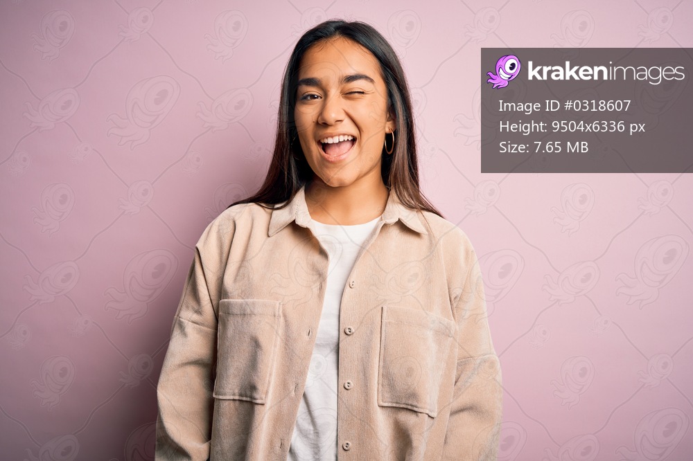 Young beautiful asian woman wearing casual shirt standing over pink background winking looking at the camera with sexy expression, cheerful and happy face.