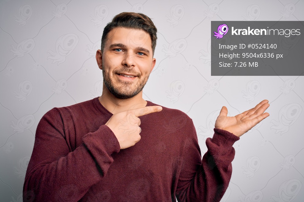 Young man with blue eyes wearing casual sweater standing over isolated background amazed and smiling to the camera while presenting with hand and pointing with finger.