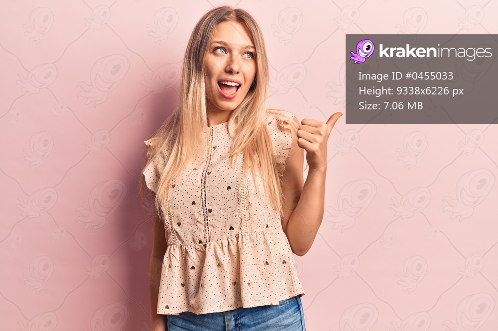 Young blonde woman wearing casual clothes pointing thumb up to the side smiling happy with open mouth 