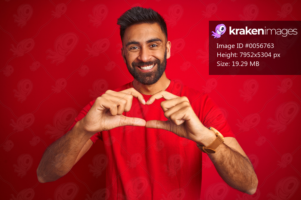 Young handsome indian man wearing t-shirt over isolated red background smiling in love showing heart symbol and shape with hands. Romantic concept.