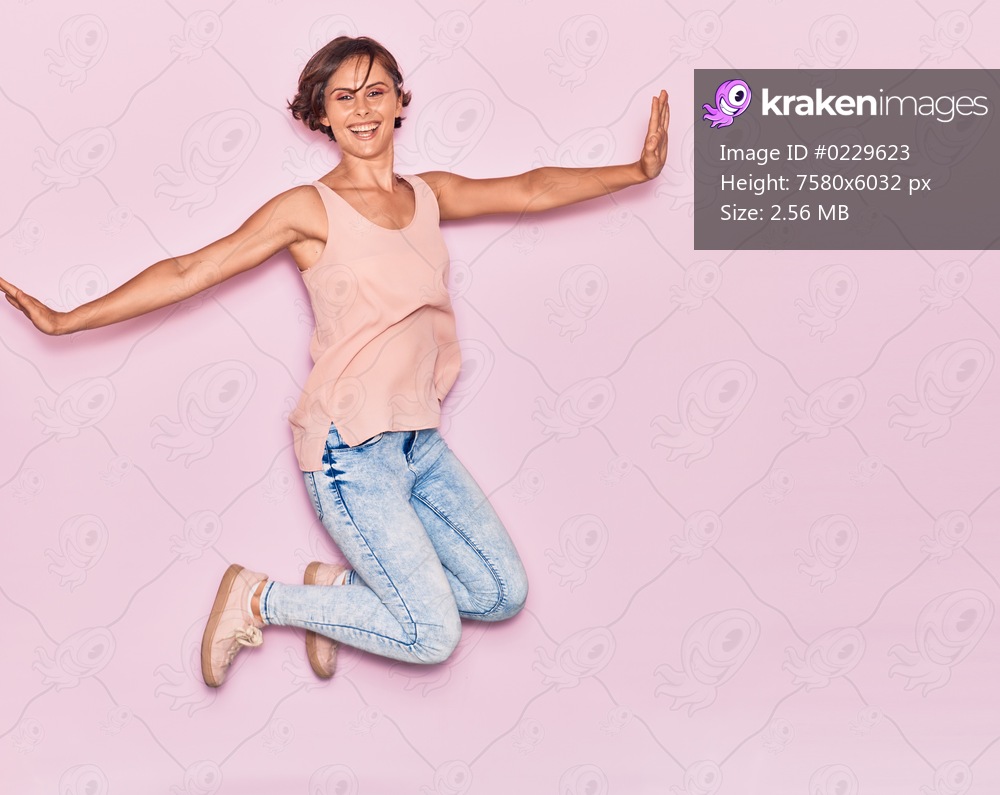 Young beautiful woman wearing casual clothes smiling happy. Jumping with smile on face and arms opened over isolated pink background.