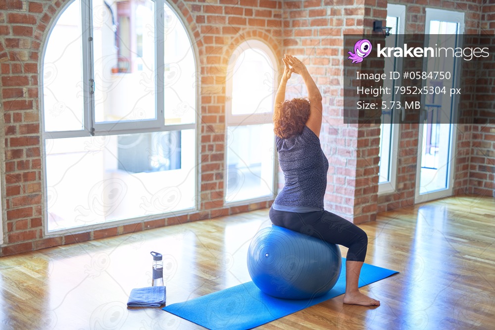 Middle age beautiful sportswoman doing exercise using fitness ball in a class of yoga at gym