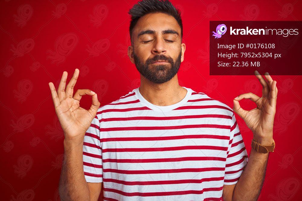 Young indian man wearing striped t-shirt standing over isolated red background relax and smiling with eyes closed doing meditation gesture with fingers. Yoga concept.