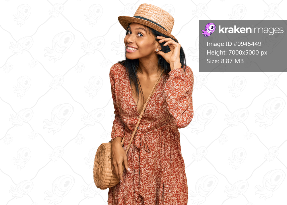 Young african american woman wearing summer hat smiling with hand over ear listening an hearing to rumor or gossip. deafness concept. 