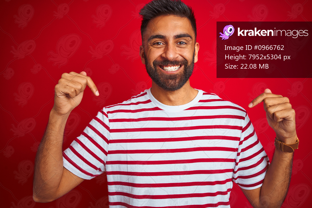 Young indian man wearing striped t-shirt standing over isolated red background looking confident with smile on face, pointing oneself with fingers proud and happy.
