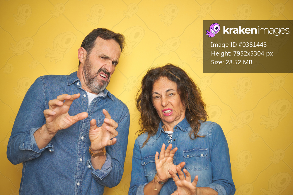 Beautiful middle age couple together standing over isolated yellow background disgusted expression, displeased and fearful doing disgust face because aversion reaction. With hands raised. Annoying concept.