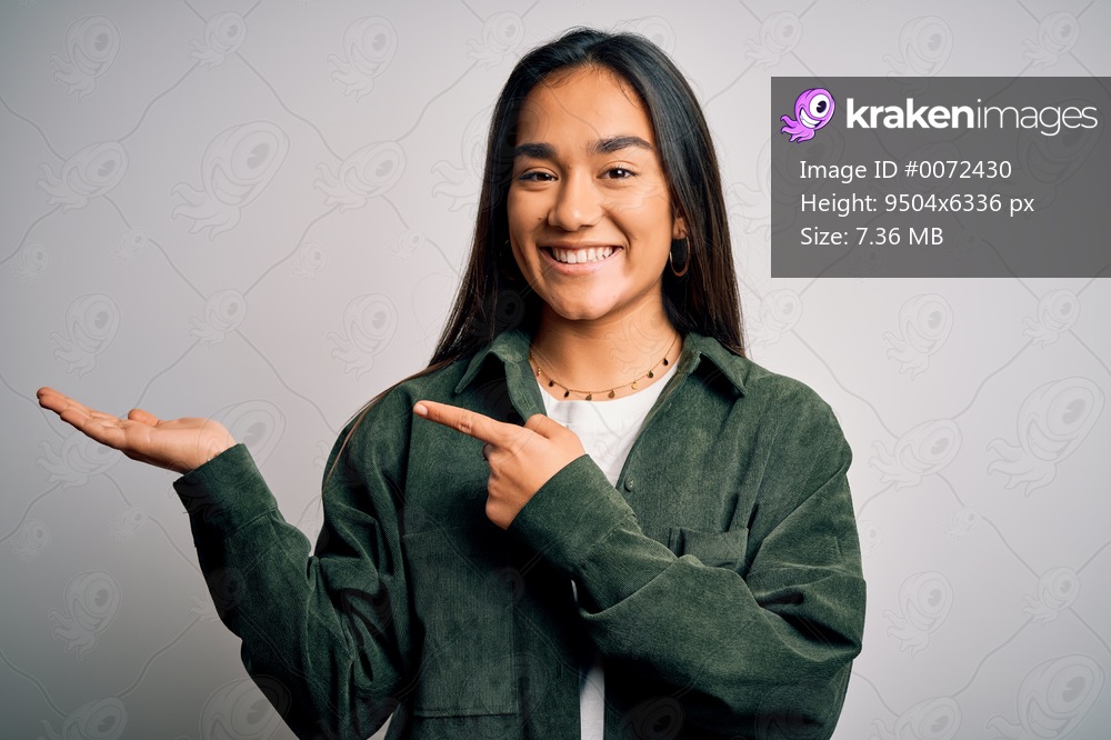 Young beautiful asian woman wearing casual shirt standing over isolated white background amazed and smiling to the camera while presenting with hand and pointing with finger.