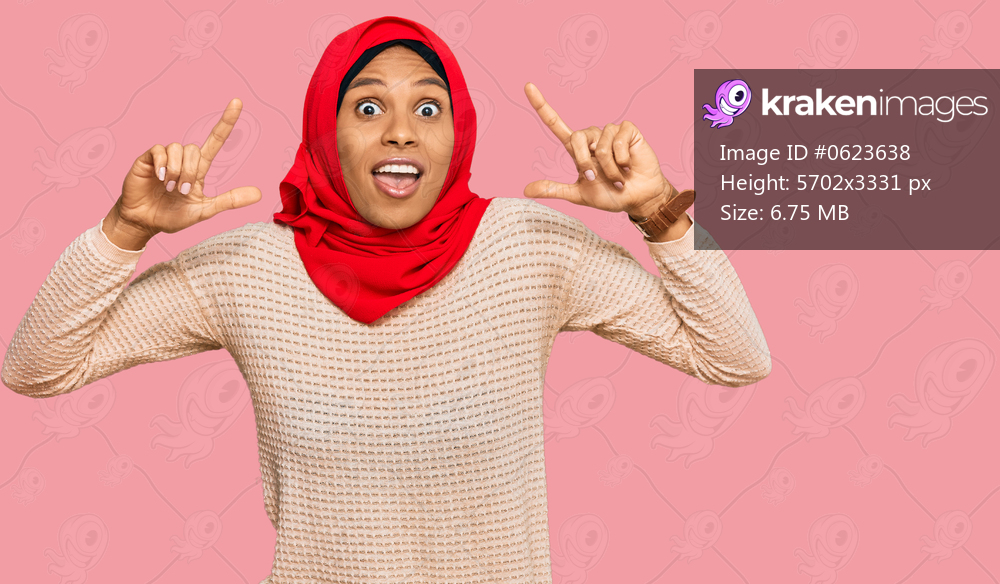 Young african american woman wearing traditional islamic hijab scarf smiling amazed and surprised and pointing up with fingers and raised arms. 