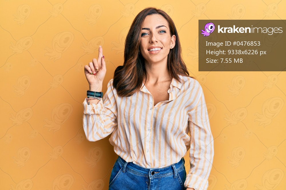 Young brunette woman wearing casual clothes over yellow background smiling with an idea or question pointing finger up with happy face, number one 