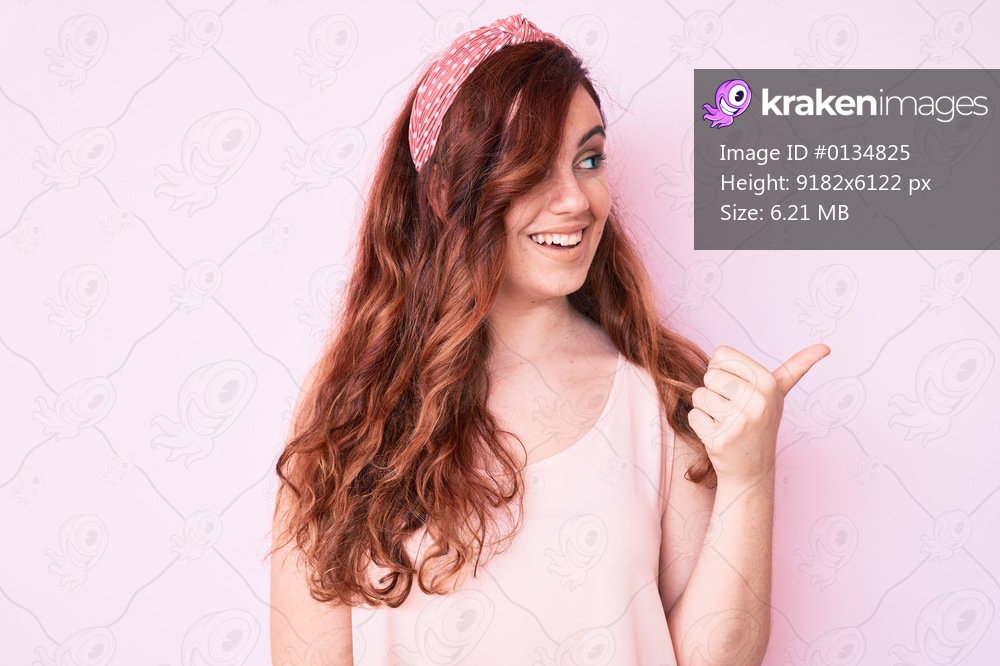 Young beautiful woman wearing casual clothes smiling with happy face looking and pointing to the side with thumb up. 