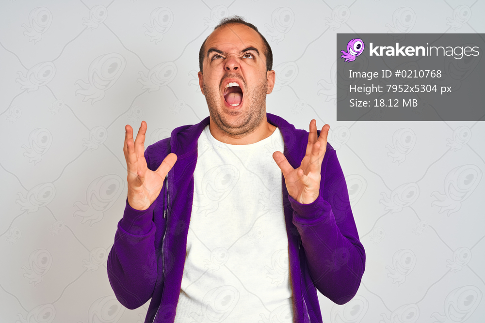Young man wearing purple sweatshirt standing over isolated white background crazy and mad shouting and yelling with aggressive expression and arms raised. Frustration concept.